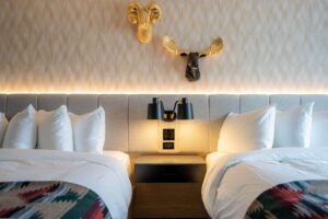 Two beds with plush white bedding in a hotel room with decorative ram and moose heads.