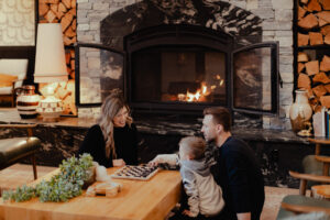 Family playing checkers by a stone fireplace, promoting a cozy stay.