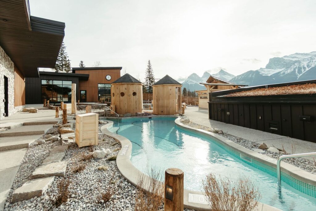 Everwild spa exterior with outdoor pool, wooden saunas, and mountain backdrop near Calgary.