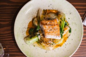 Pan-seared fish with bok choy and orange sauce on a speckled plate.