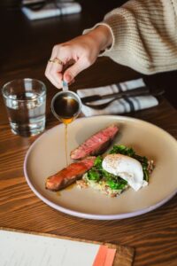 Pouring sauce over steak, greens, and poached egg on a plate
