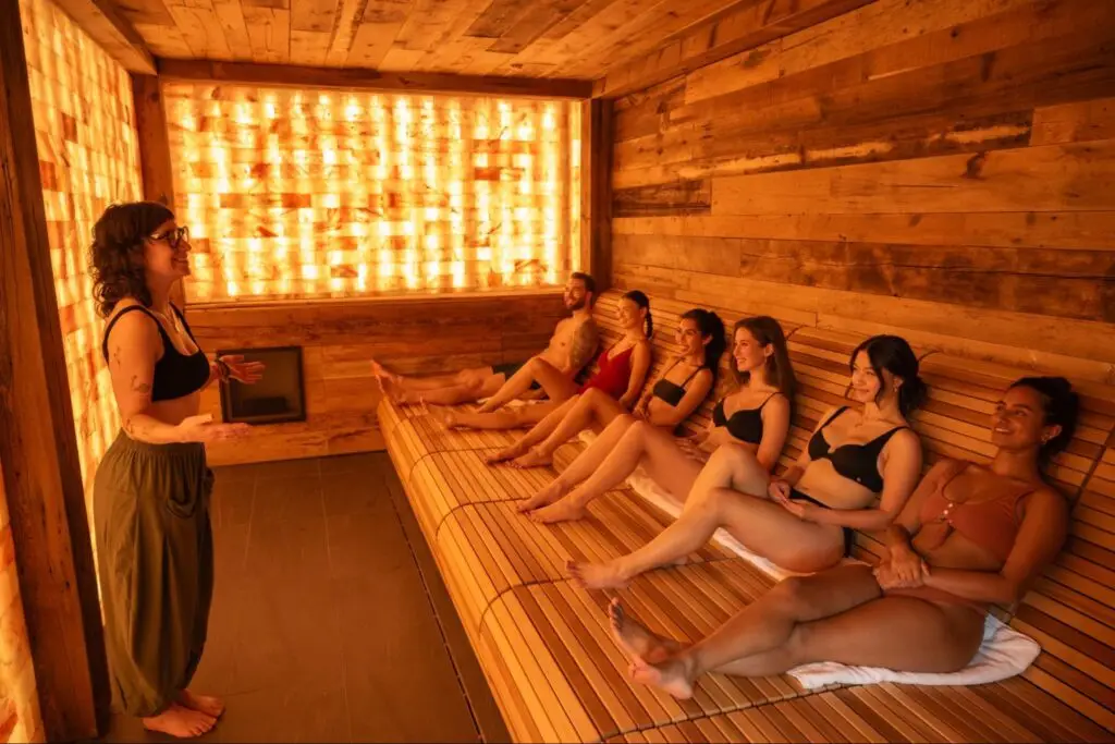People relaxing in a warm, wood-paneled sauna with a salt wall, promoting wellness.