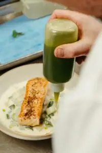 Chef garnishes salmon with green sauce in a creamy dish